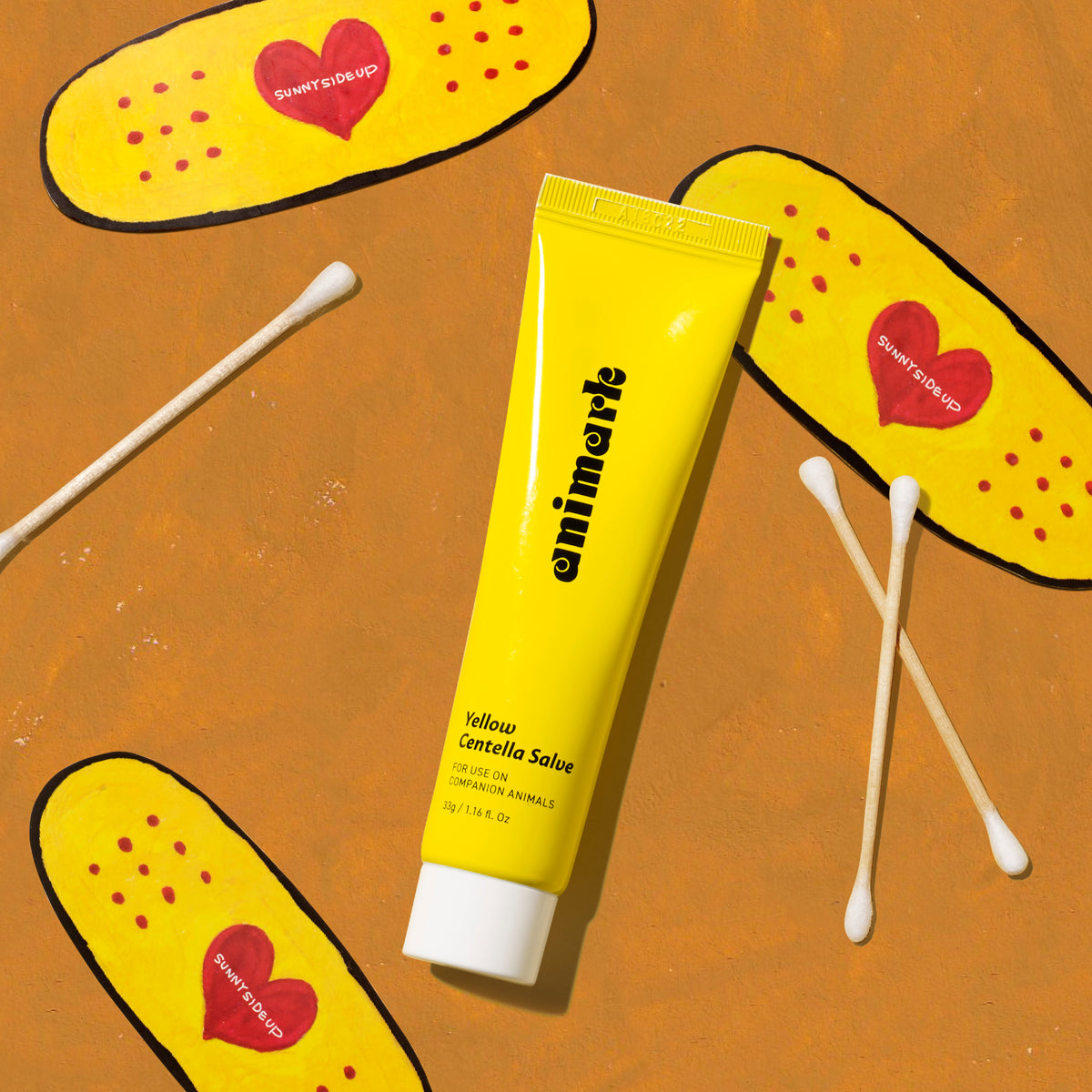 Yellow tube of emimerk Centella Salve on an orange background with cartoon bandages and cotton swabs.
